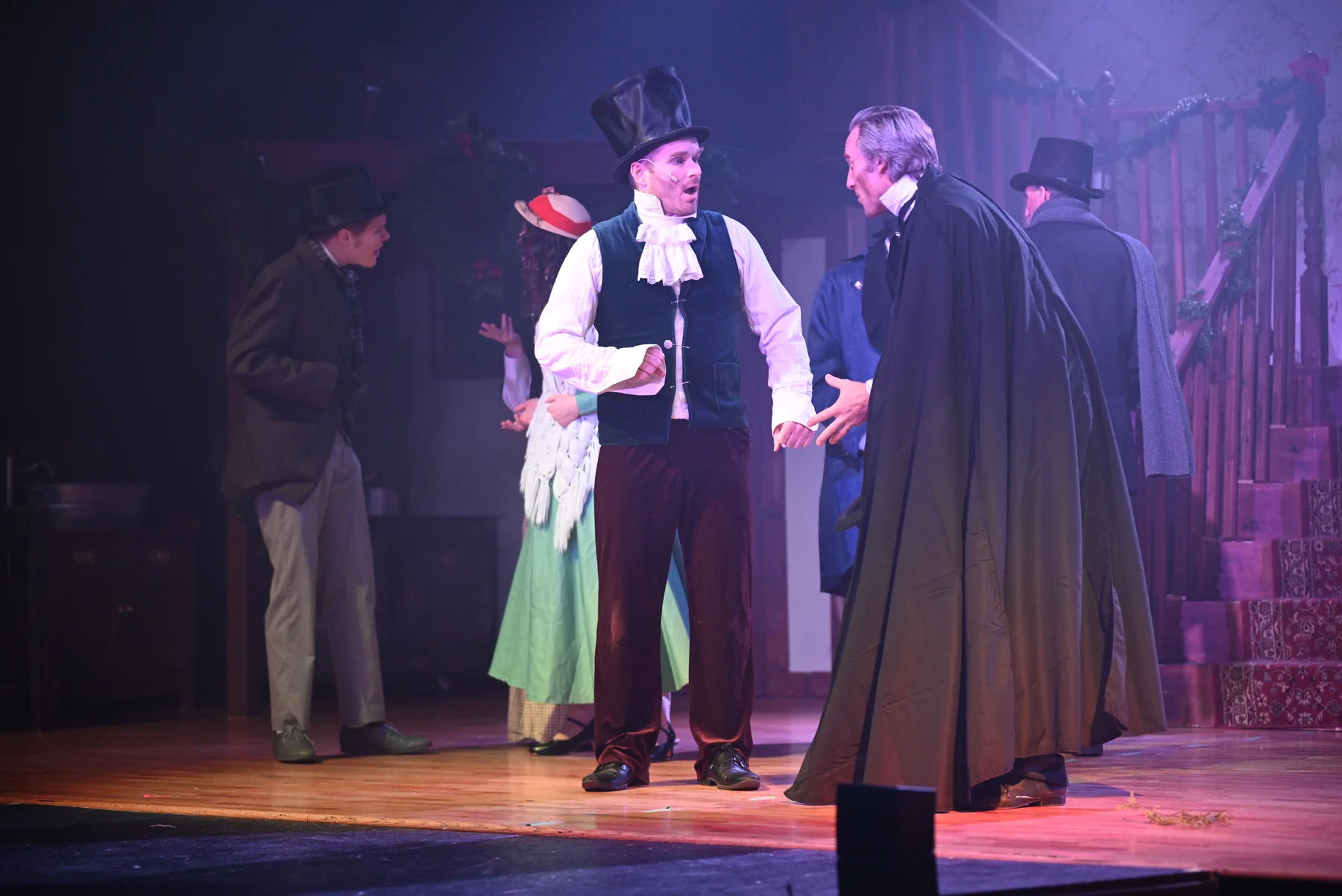 A smiling Scrooge shares an animated exchange with a boy in the 2025 production.